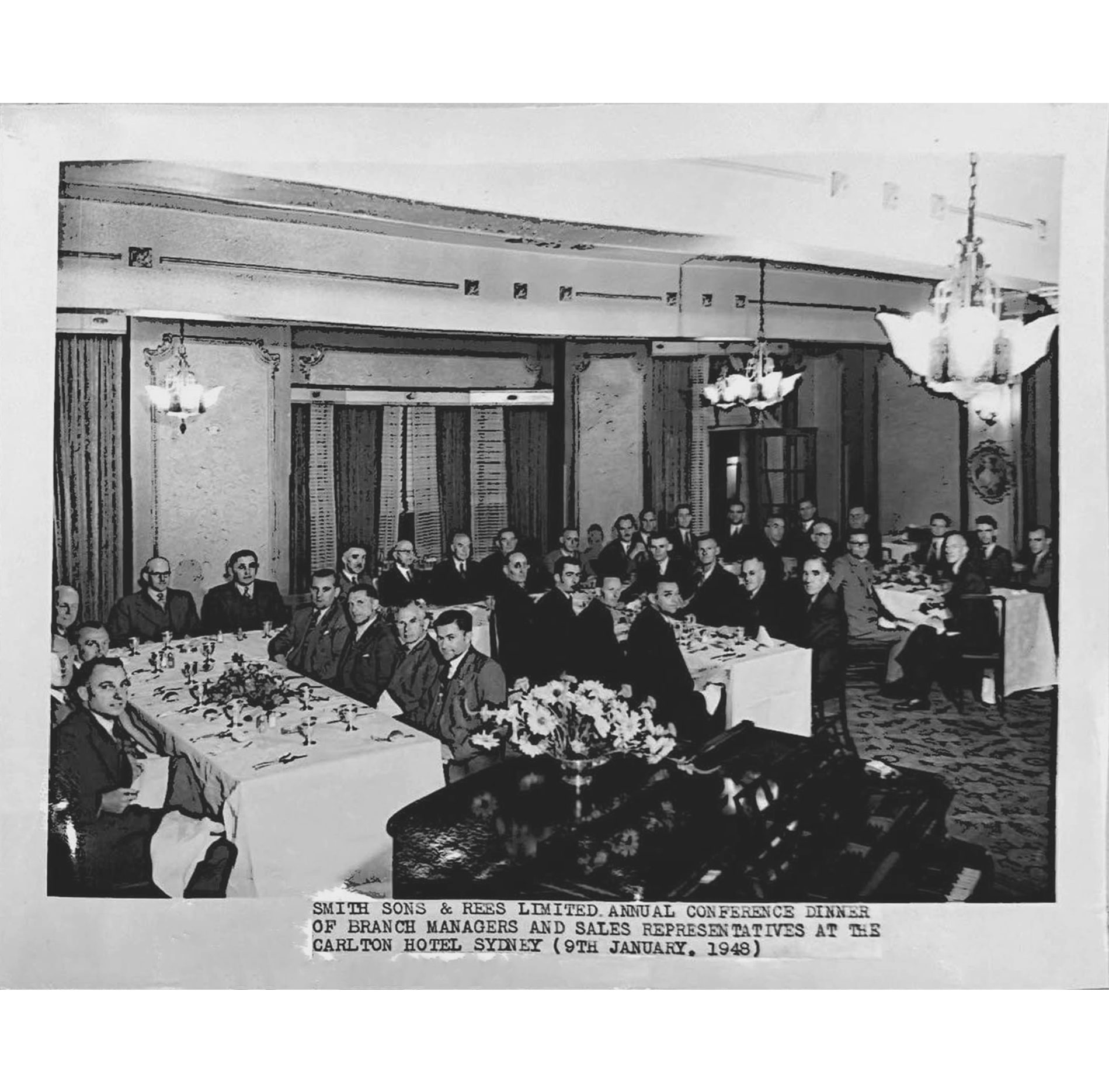 A black a white photograph of men in suits sitting at dining tables in a conference room.